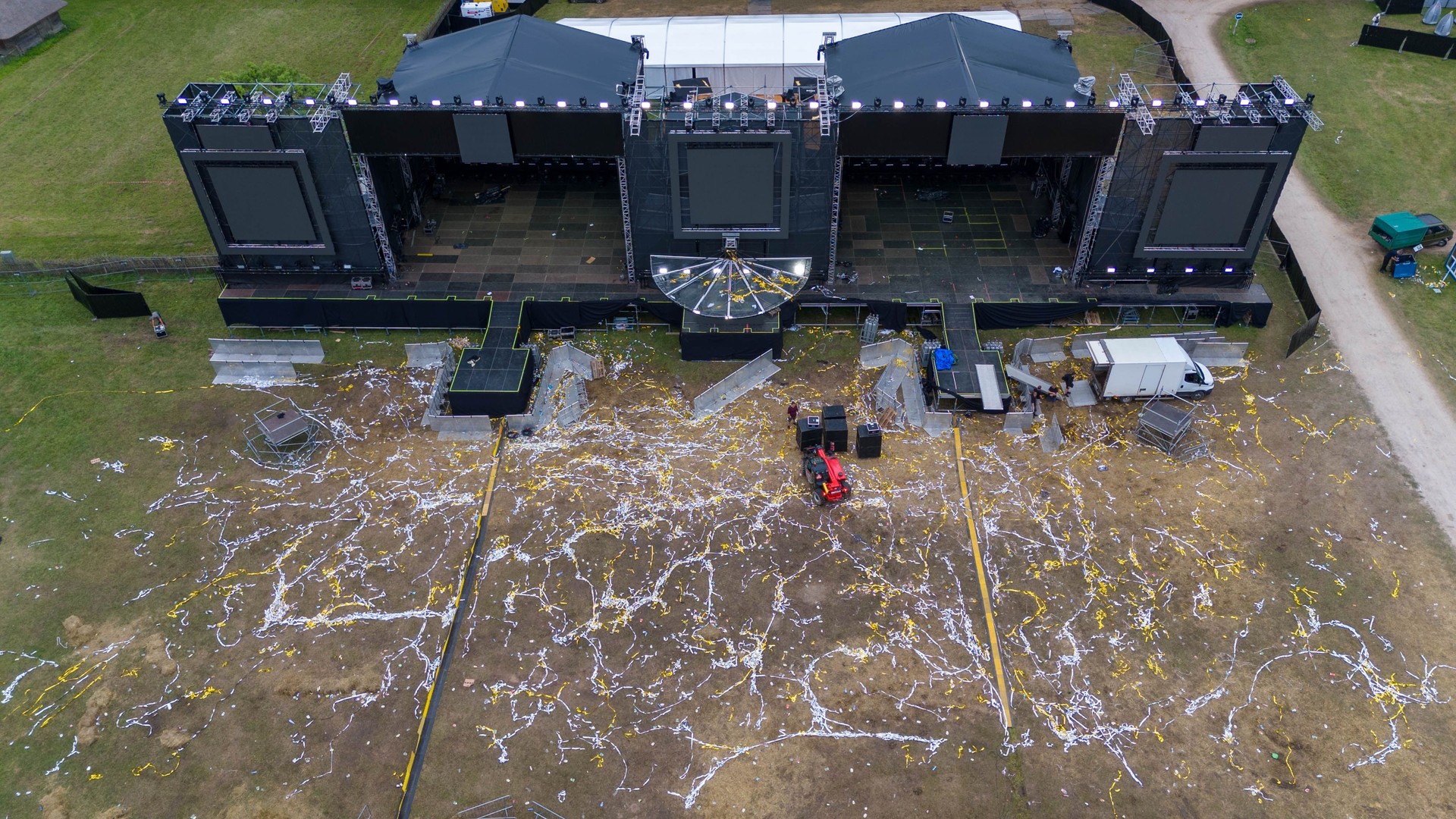 Drone photography of volunteers cleaning up trash and people dismantling music scene after music festival during summer day